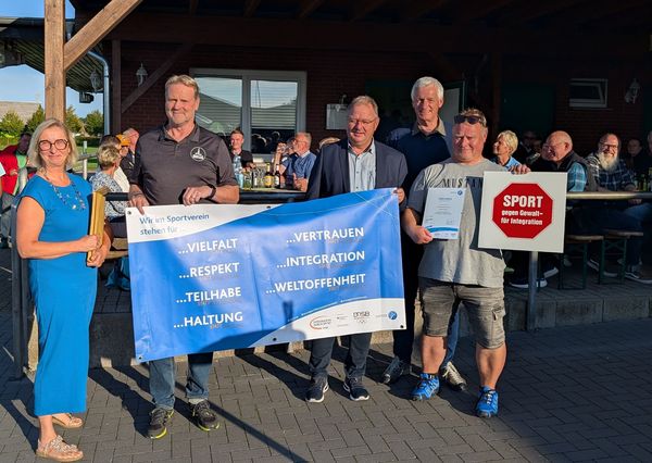 4 Personen lächeln und stehen vor einer Gruppe Menschen. Sie halten ein blaues Banner für Integration im Sport